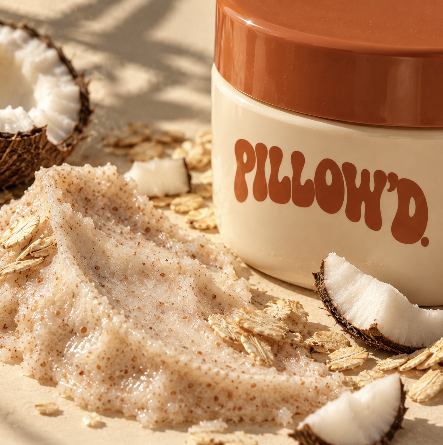 A Pillow'd scrub jar beside a smear of exfoliant, rolled oats and coconut pieces