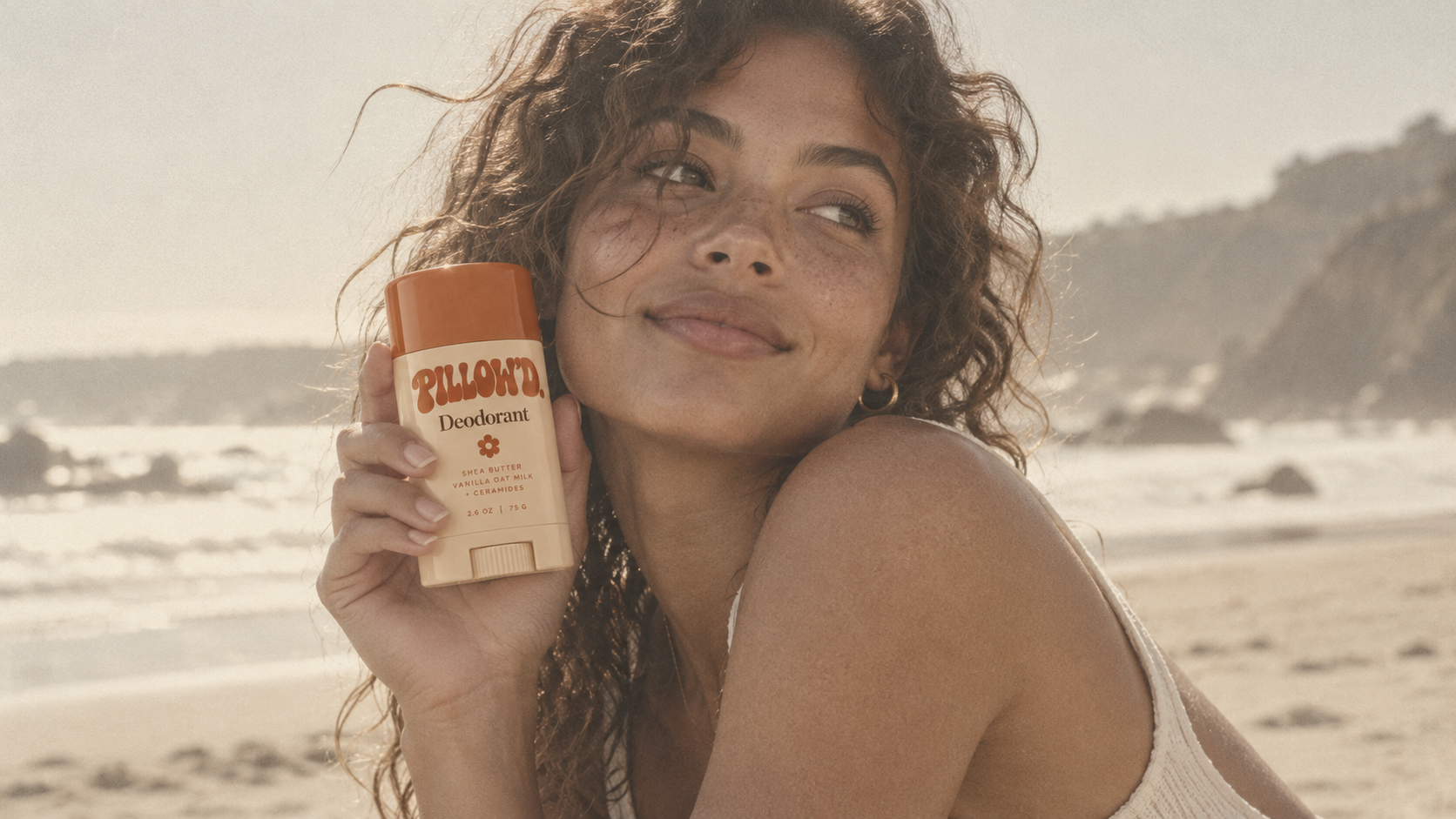Pillow’d Deodorant held beside a smiling woman on a sunlit beach
